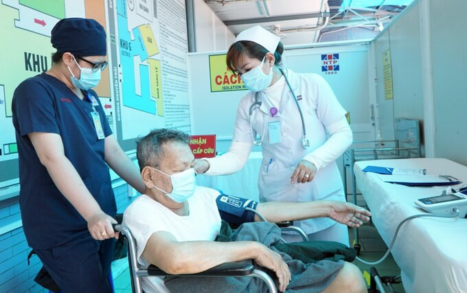 Nhân viên y tế đo nhiệt độ, hỗ trợ khai báo y tế cho bệnh nhân ưu tiên tại buồng sàng lọc riêng, Bệnh viện Nguyễn Tri Phương. Ảnh:Thư Anh.