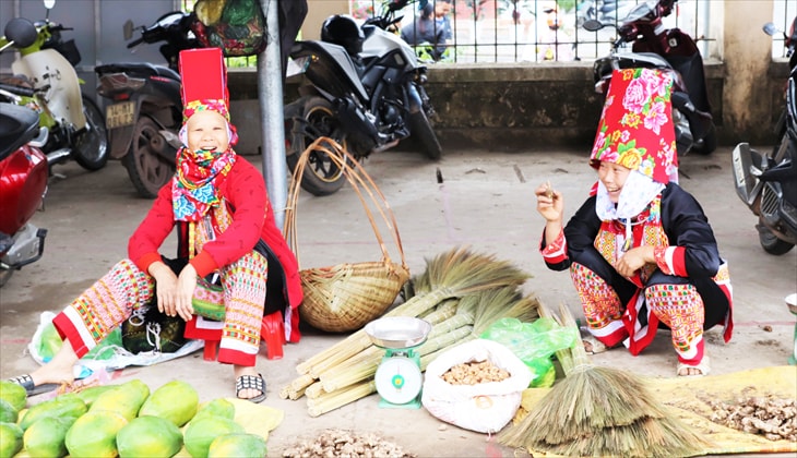 Phụ nữ Dao Thanh Phán rực rỡ trong trang phục truyền thống, bày bán hoa quả, vật dụng trong gia đình do chính mình làm ra tại chợ phiên. 