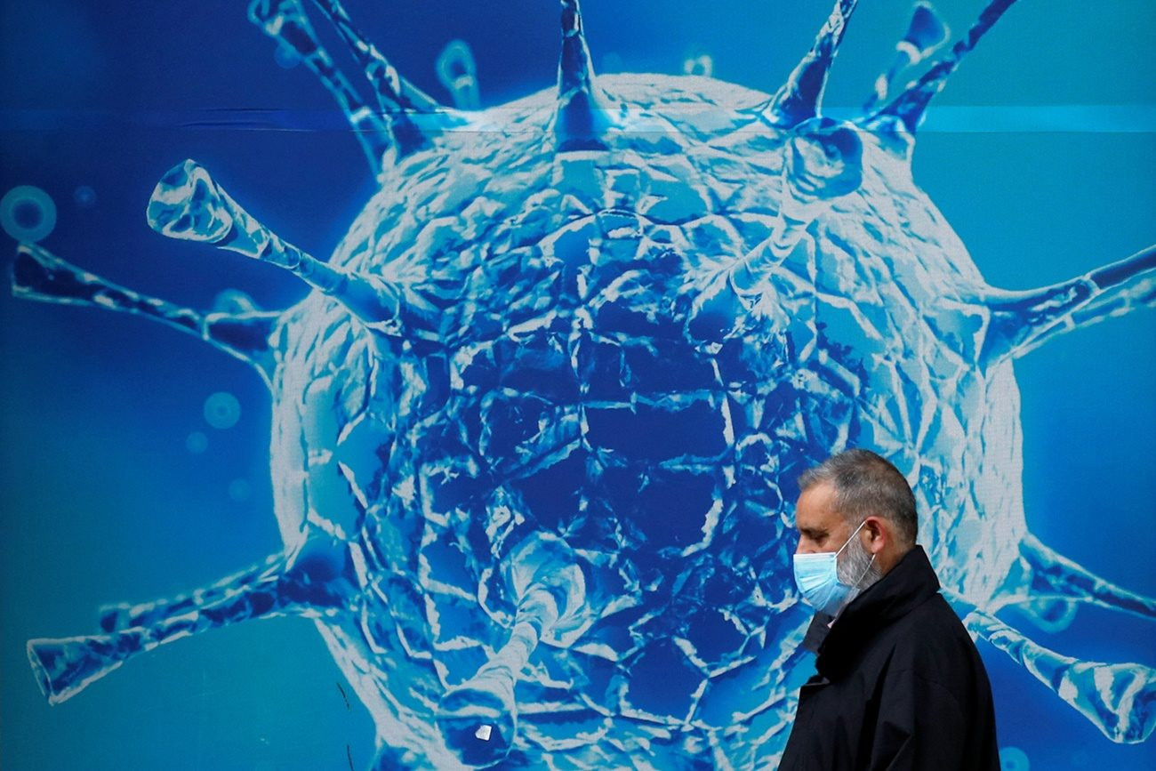 a_man_wearing_a_protective_face_mask_walks_past_an_illustration_of_a_virus_in_amid_covid_19_outbreak_in_oldham_britain_uk_august_3_2020_reuters_.jpg