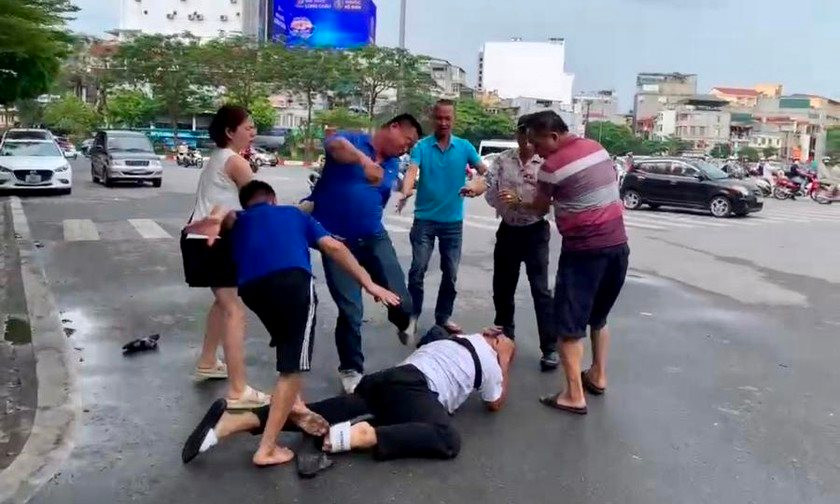 Hình ảnh phóng viên nằm gục xuống đường vẫn bị hai người đàn ông mặc áo xanh tấn công.