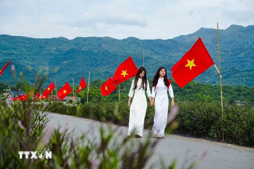 Hai nữ sinh trong trang phục áo dài giữa không gian rực rỡ cờ Tổ quốc trên cánh đồng Mường Thanh. (Ảnh: Xuân Tư/TTXVN)